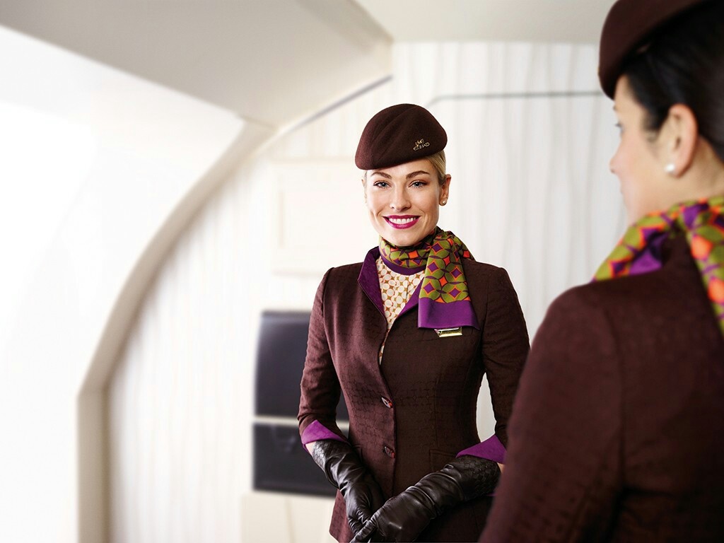 безумно красивая девушка - бортпроводница Etahad Airways в кабине самолета в фирменно одежде улыбается