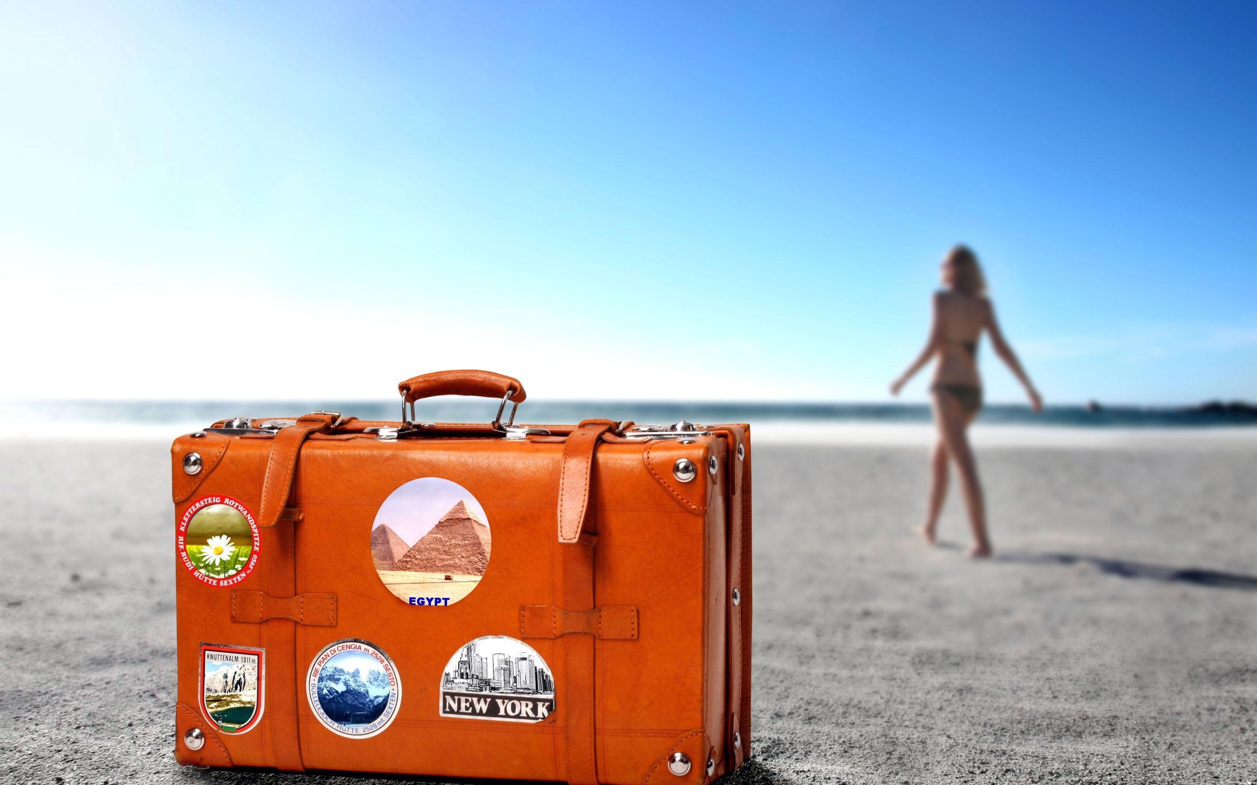 туристический чемодан, девушка в купальнике идет по пляжу