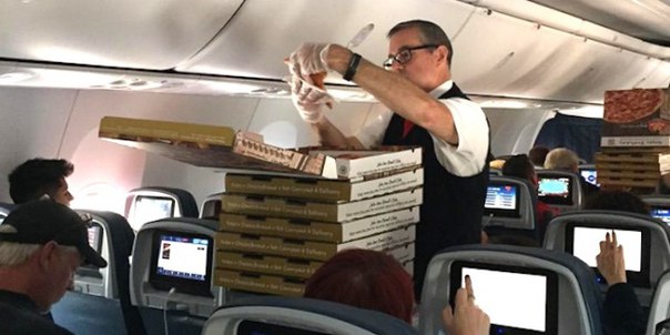 мужчина бортпроводник разносит пиццу в салоне самолета - еда на борту - красивый парень стюард