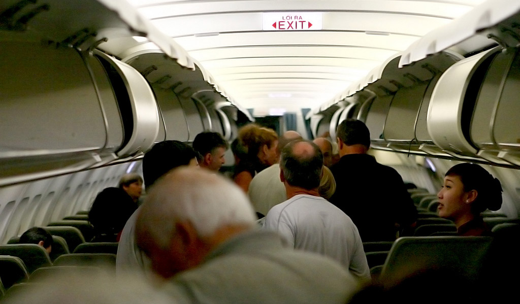 толпа пассажиров в проходе салона самолета ожидает выхода в аэропорт после посадки воздушного судна
