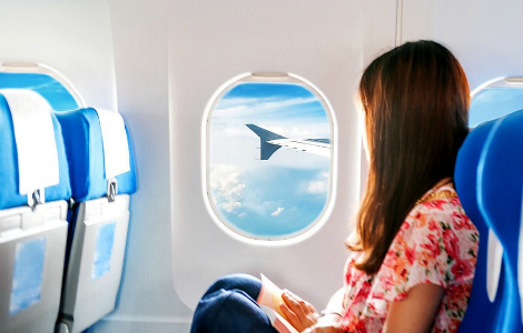 красивый вид из окна самолета - девушка смотрит в юллюминатор на голубое небо с облаками